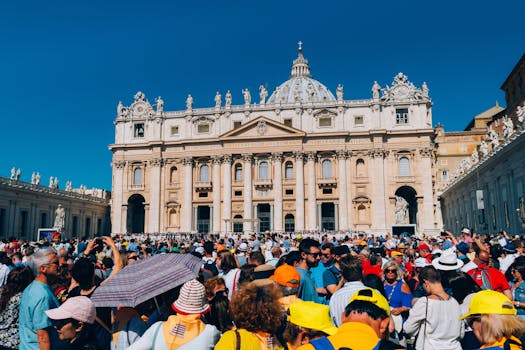 A large crowd gathers outside St. Peter's Basilica under a clear blue sky.